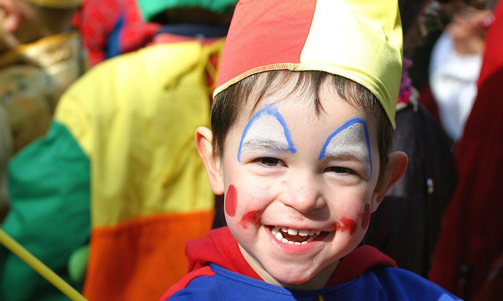 kleiner Junge als Clown verkleidet in einer Menschenmenge draußen