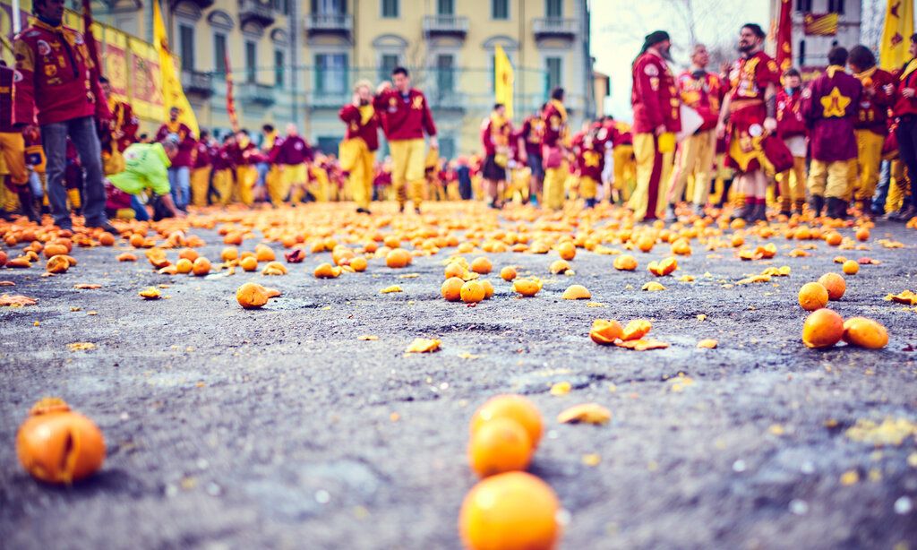 Karneval in Ivrea, Orangenschlacht, sehr viele Orangen liegen auf einem Platz in Ivrea, verkleidete Männer sthen herum