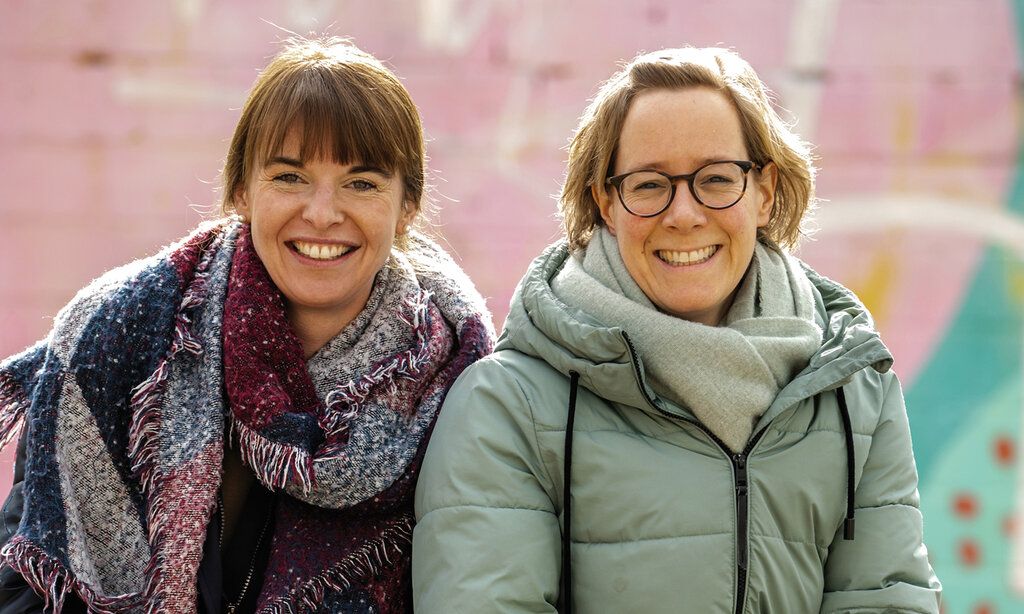 Die Gründerinnen der Initiative Kleeblatt Simone Eßer und Eva Schwientek vor einer Mauer, die rosa und türkis angemalt ist