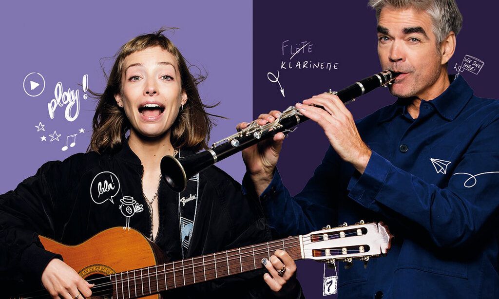 eine Frau spielt Gitarre und ein Mann Klarinette, der Hintergrund ist links hell- und rechts dunkelviolett