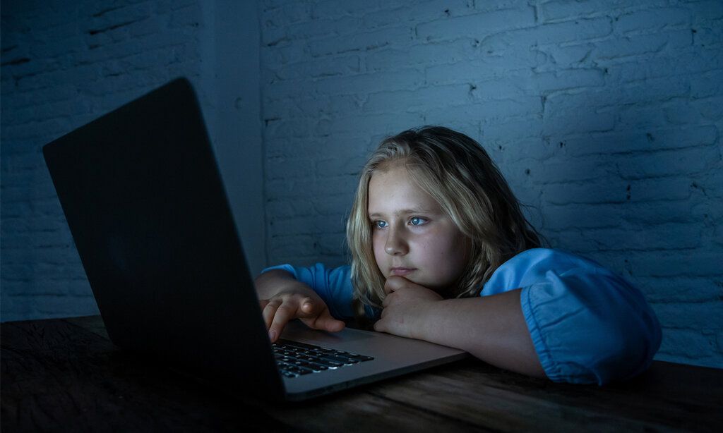 Mädchen sitz in einem dunlen Zimmer und guckt auf den leuchtenden Bildschirm eines Laptops