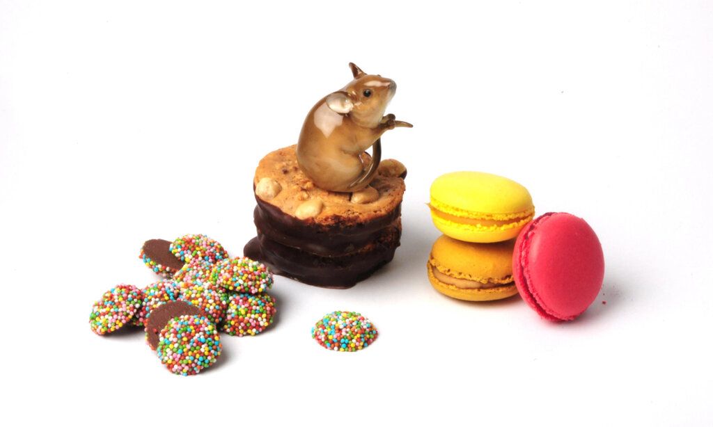 Verschiedene Süßigkeitenauf weißem Grund: Schokotaler mit Perlen, Erdnusskeks, Macarons, auf dem Plätzchen sitzt eine Porzellanmaus