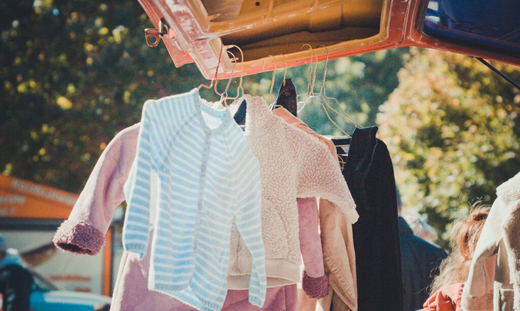 gebrauchte Kinderkleidung hängt an der geöffneten Heckklappe eines Transporters, sonnige Stimmung