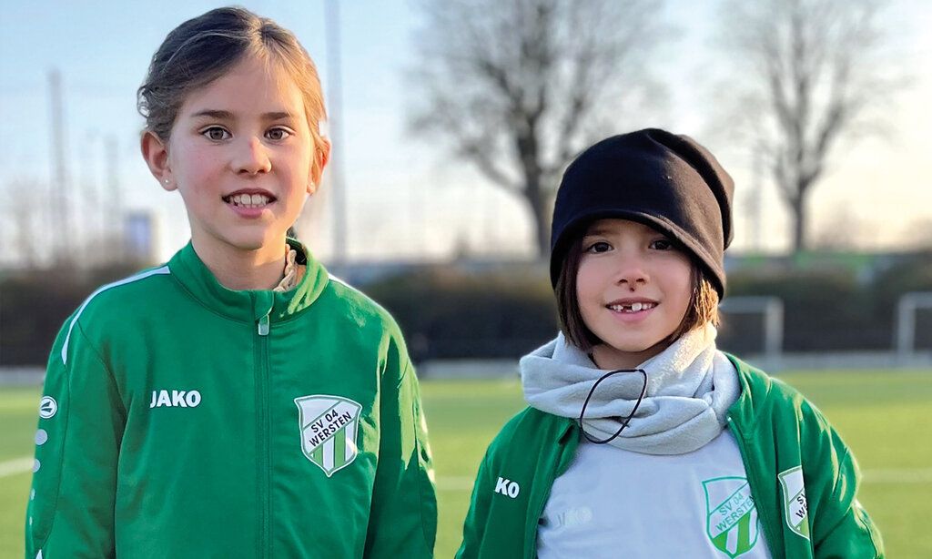 Zwei Mädchen in Fußballtrikots stehen auf einem Fußballplatz