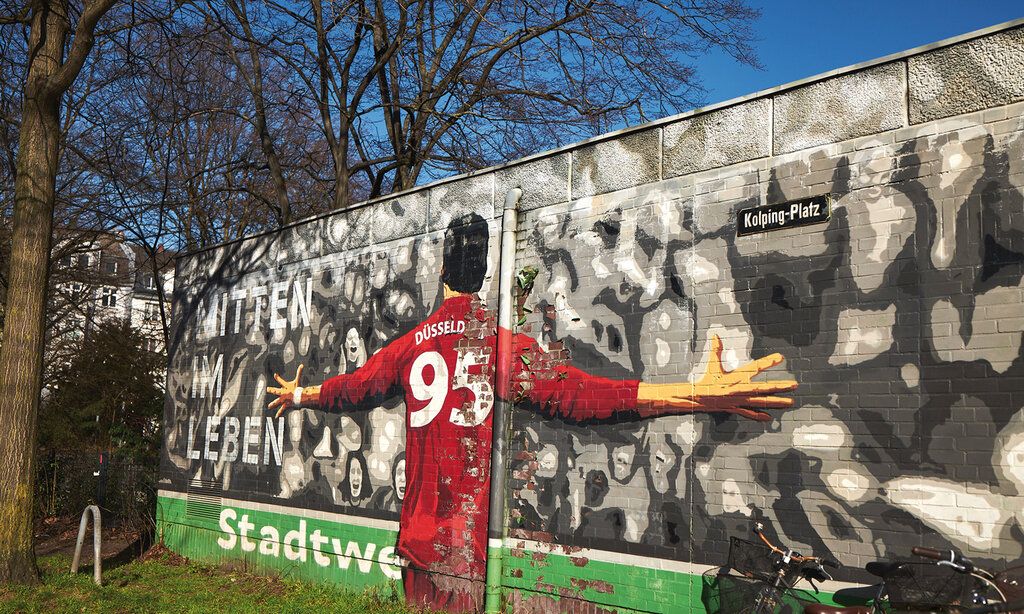 Graffiti an der Mauer am Düsseldorfer Kolping Platz, Motiv: Fortuna Fußballspieler, Schrift: Mitten im Leben, Stadtwerke