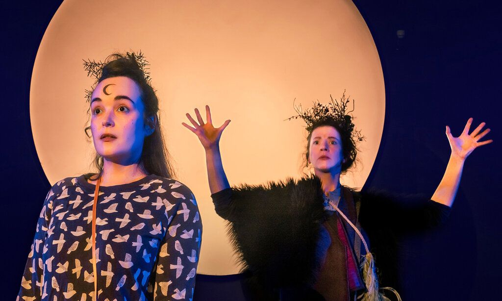 zwei Schauspielerinnen vor einem großen hellen Kreis, der den Mond darstellt