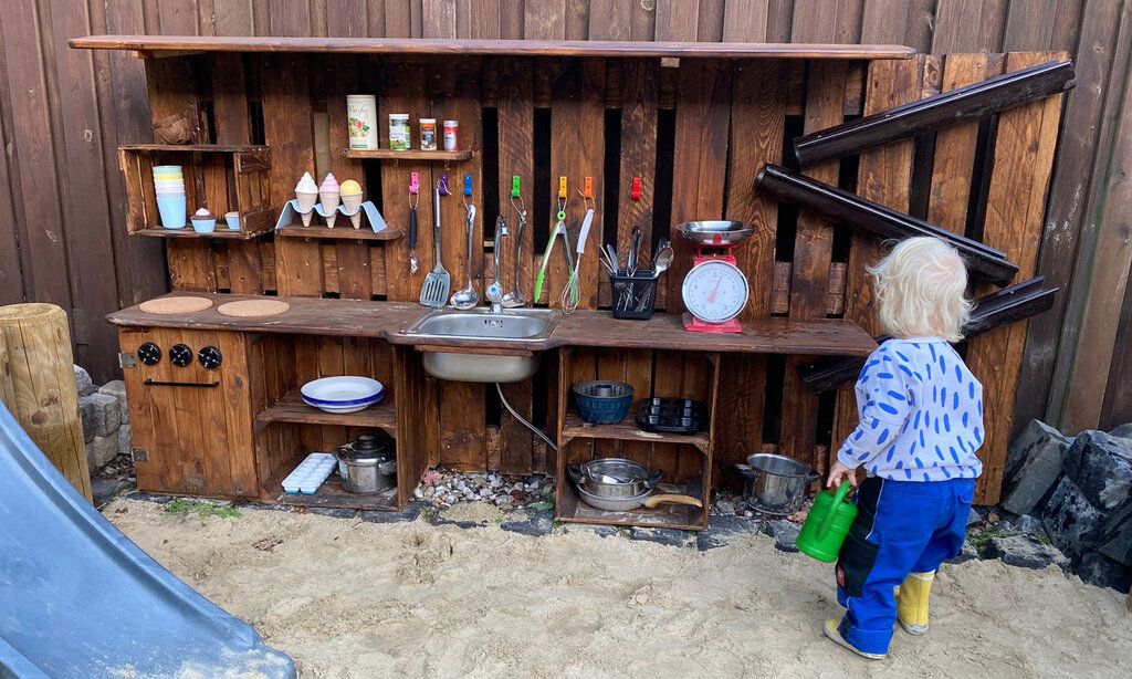 Kleinkind spielt in selbstgebauter Spielküche.