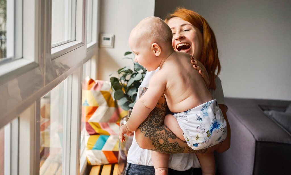 Junge Frau trägt Baby auf dem Arm, das eine Stoffwindel trägt, die Mutter lacht