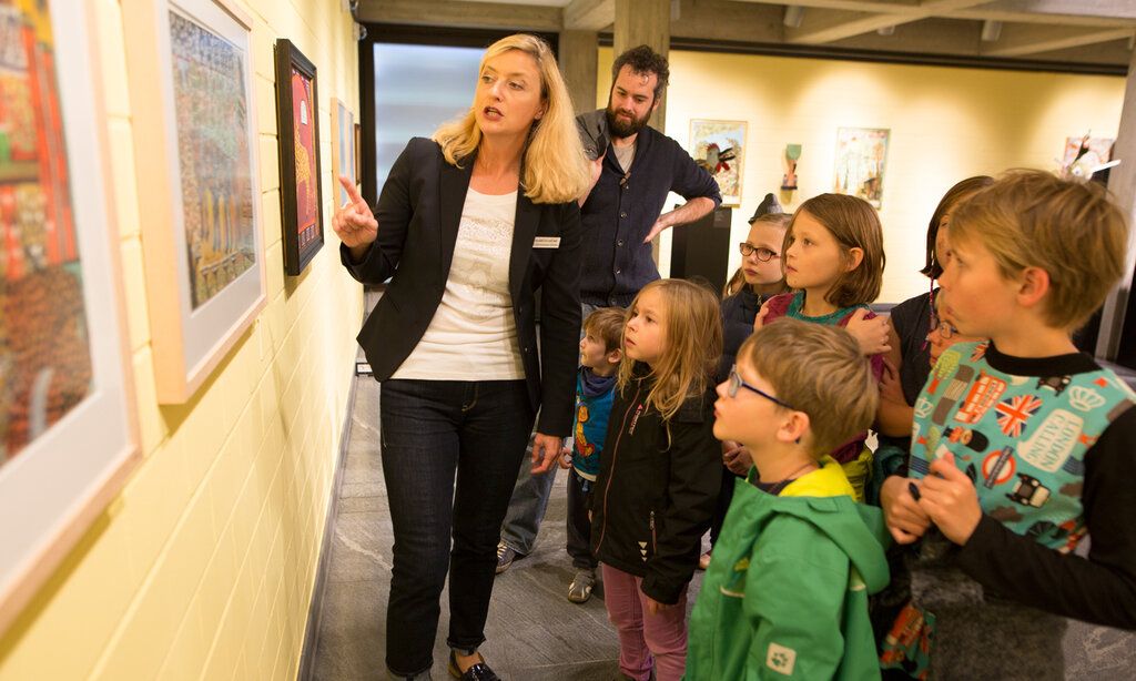 Eine Museumsführerin steht mit Kindern vor einem gemälde und erklärt es.