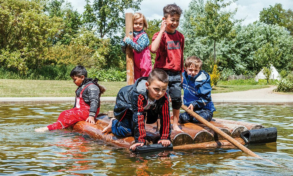 Kinder stehen auf einem Floß in einem kleinen Teich