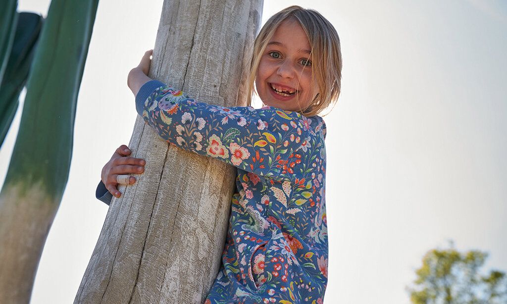 Ein Mädchen klettern auf dem Kraut-und-Rüben-Spielplatz im Südpark, umklammert lachend einen Holzbalken