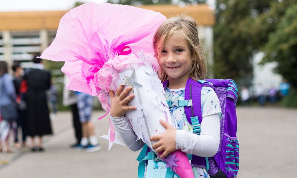 Ein Mädchen steht auf einem Schulhof und hält stolz eine rosa Schultüte im Arm