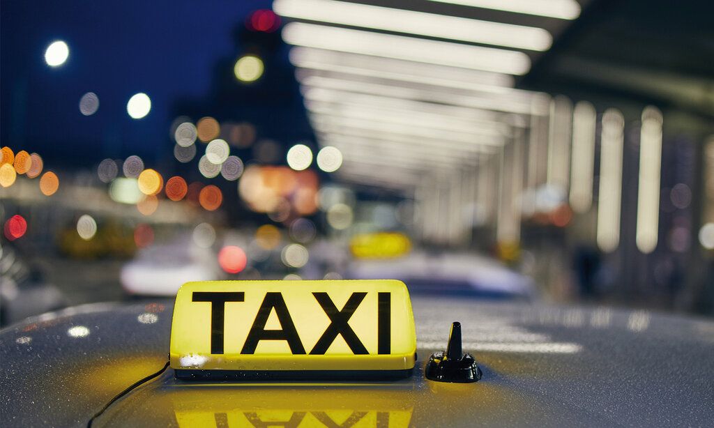 Das Dach eines Taxis mit einem leuchtenden Taxischild, im Hintergund verschwommene Lichter, Stadtszene