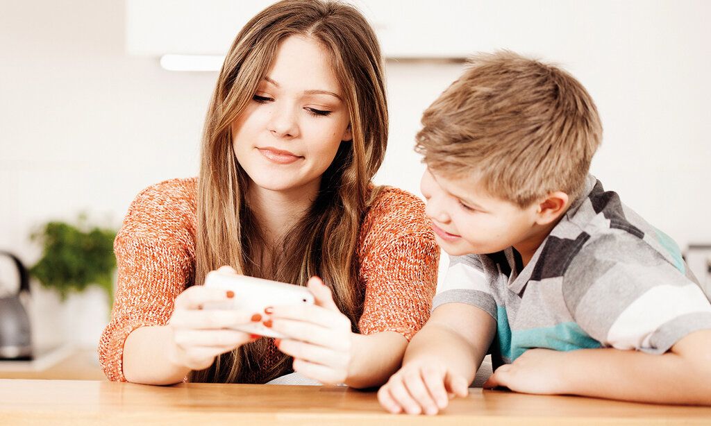 Eine Jugendliche guckt auf ihr Smartphone, ihr kleiner Bruder schaut begeistert zu