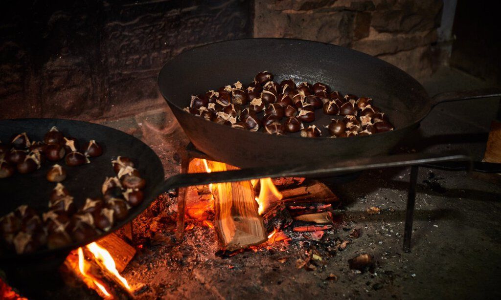 Maronen werden in gusseisernen Pfannen über offenem Feuer geröstet.