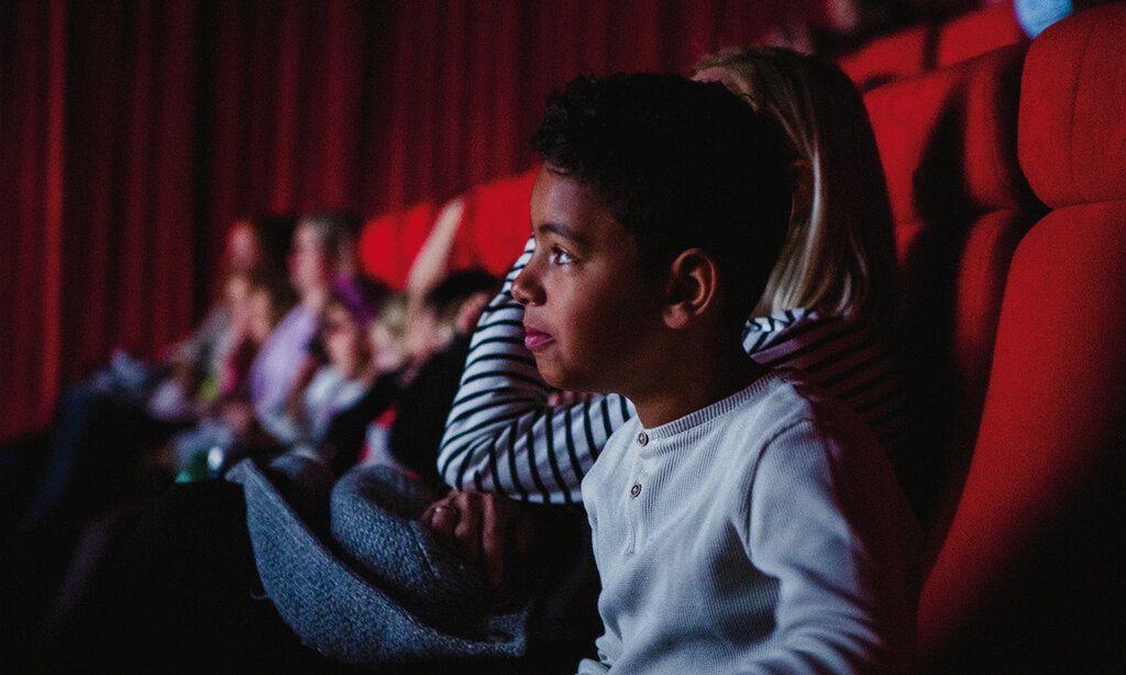 ein kleiner Junge sitzt im dunklen Kinosaal, im Hintergrund weitere Kinogäste