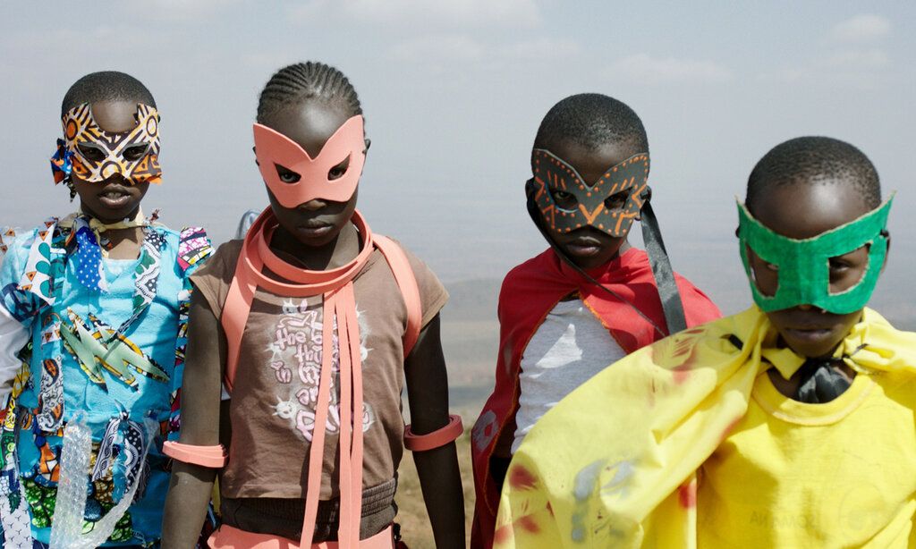 Vier schwarze Kinder laufen mit bunten Sperhelden-Masken und Umhängen  auf die Kamera zu
