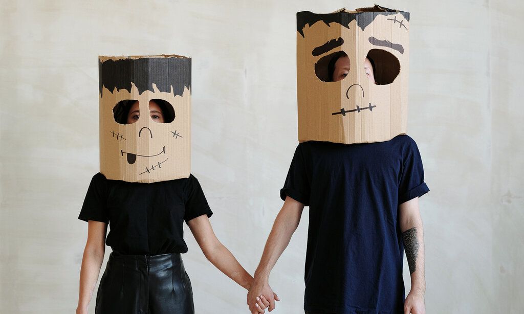 Eine Frau und ein Mann stehen nebeneinander und halten sich an den Händen, beide tragen Karton-Masken mit Frankenstein-Gesichtern bemalt