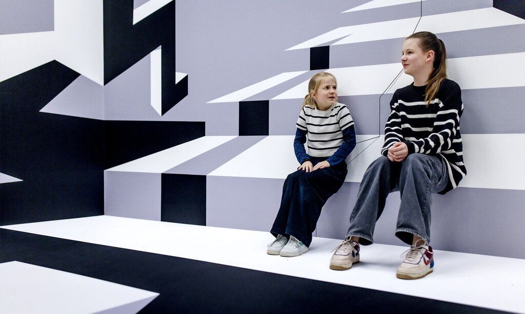 zwei Mädchen sitzen in einem grafisch gestalteten Raum im Kunstpalast