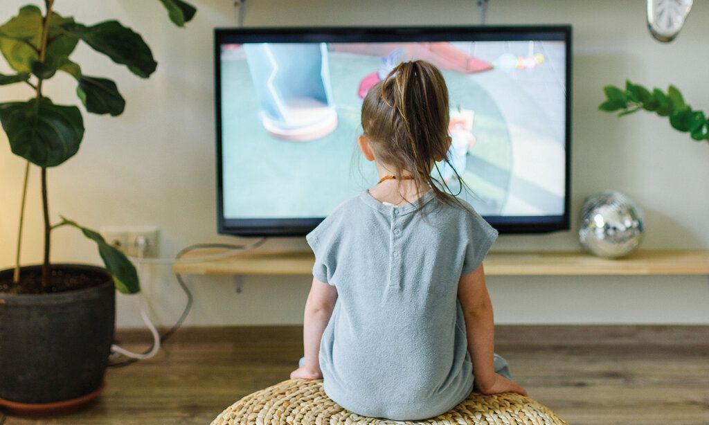 ein kleines Mädchen sitzt vor dem Fernseher, man sieht es von hinten