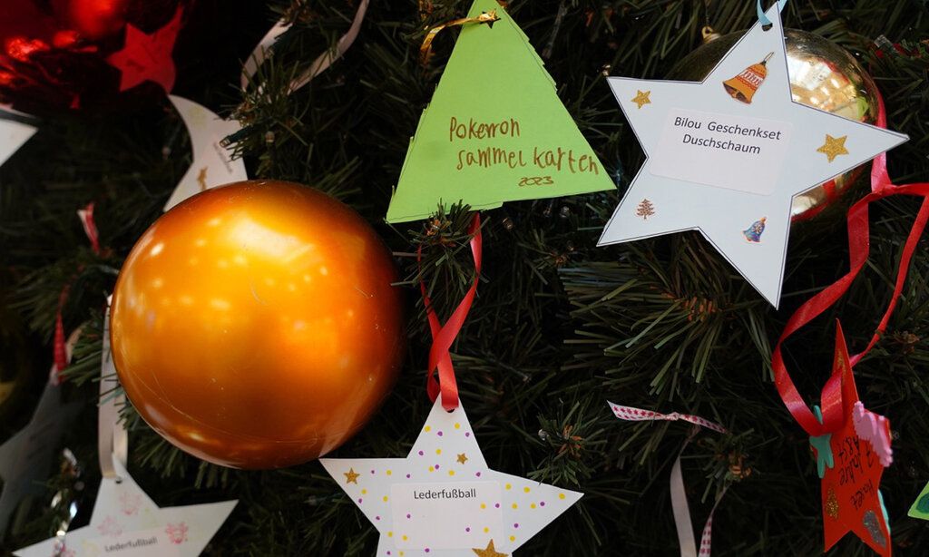 Detailansicht eines geschmückten Weihnachtsbaums mit Kugel und Papiersternen, auf denen Wünsche stehen