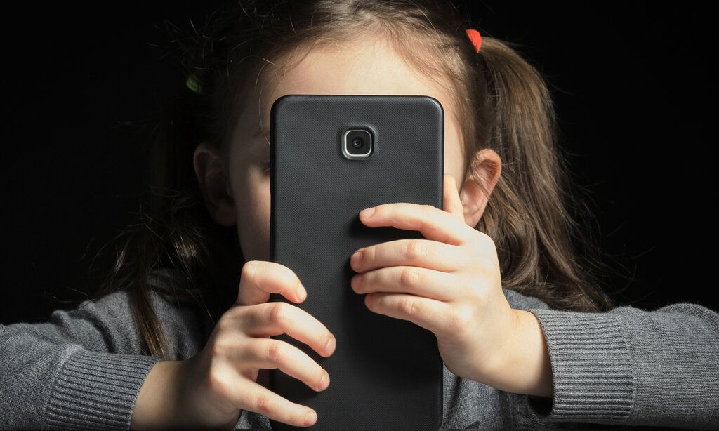 ein mädchen hält sich ein großes schwarzes Smartphone vors Gesicht