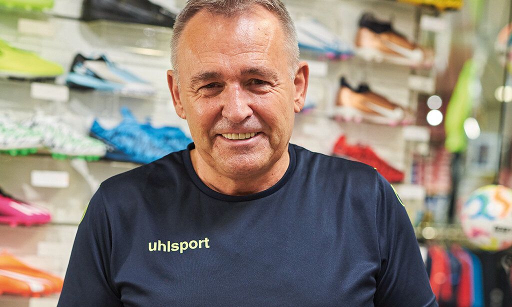ein Verkäufer von Düssel-Sport-Helmreich lächelt in die Kamera, im Hintergund bunte Sportschuhe
