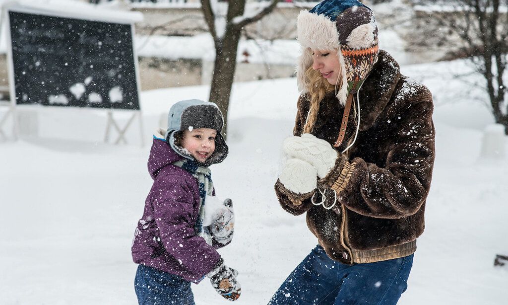 eine junge Frau und ein Kind formen Schneebälle während es schneit