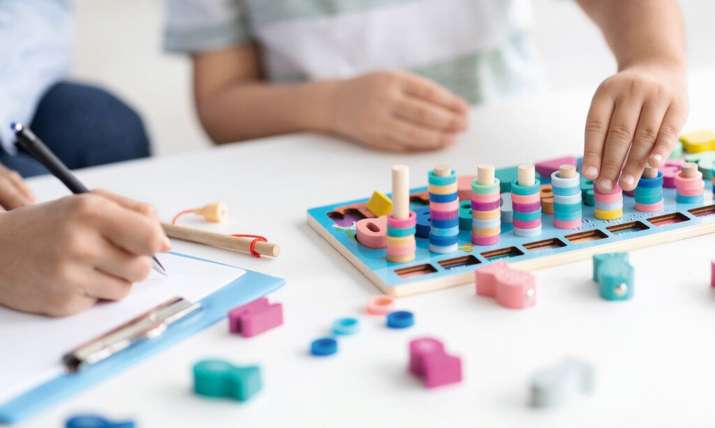 Buntes Holzspielzeug für Kinder, die Hände eines Kindes spielen damit, Ergotherapeutin macht sich Notizen
