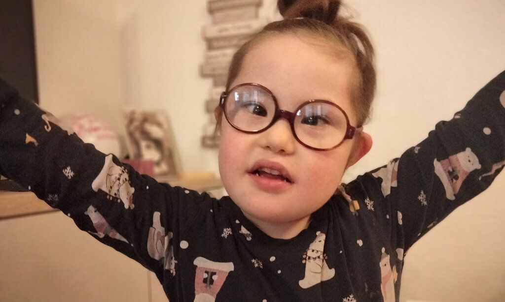 kleines Mädchen mit Down Syndrom und Brille guckt in die Kamera