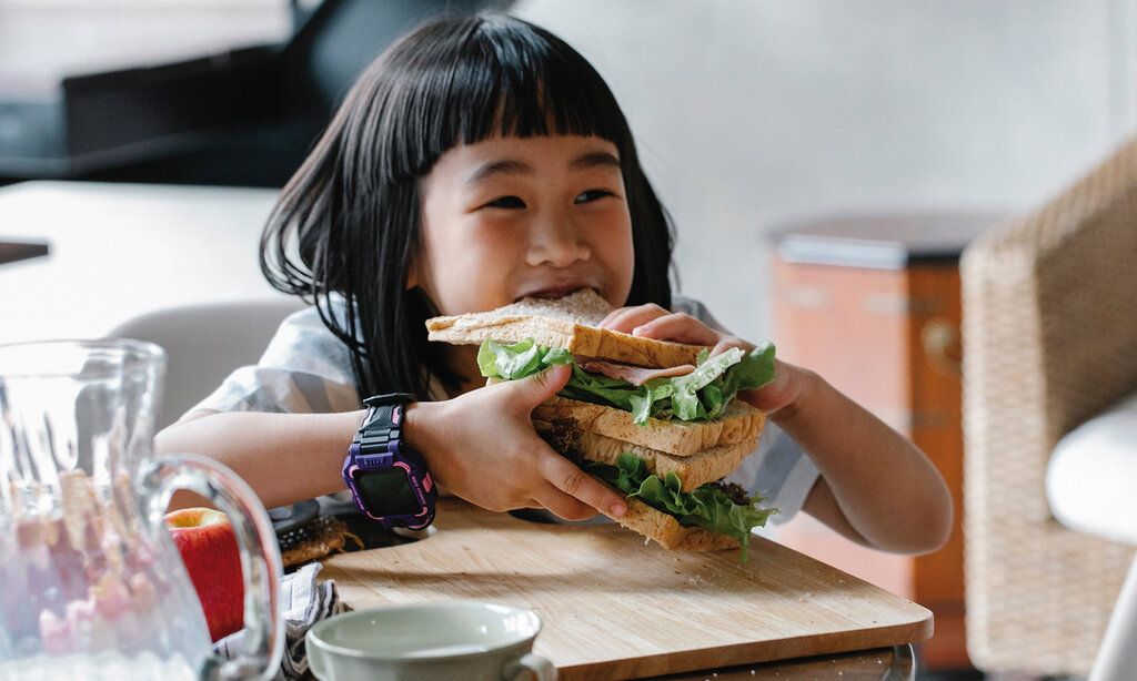 asiatisches Mädchen beißt in ein sehr großes Sandwich