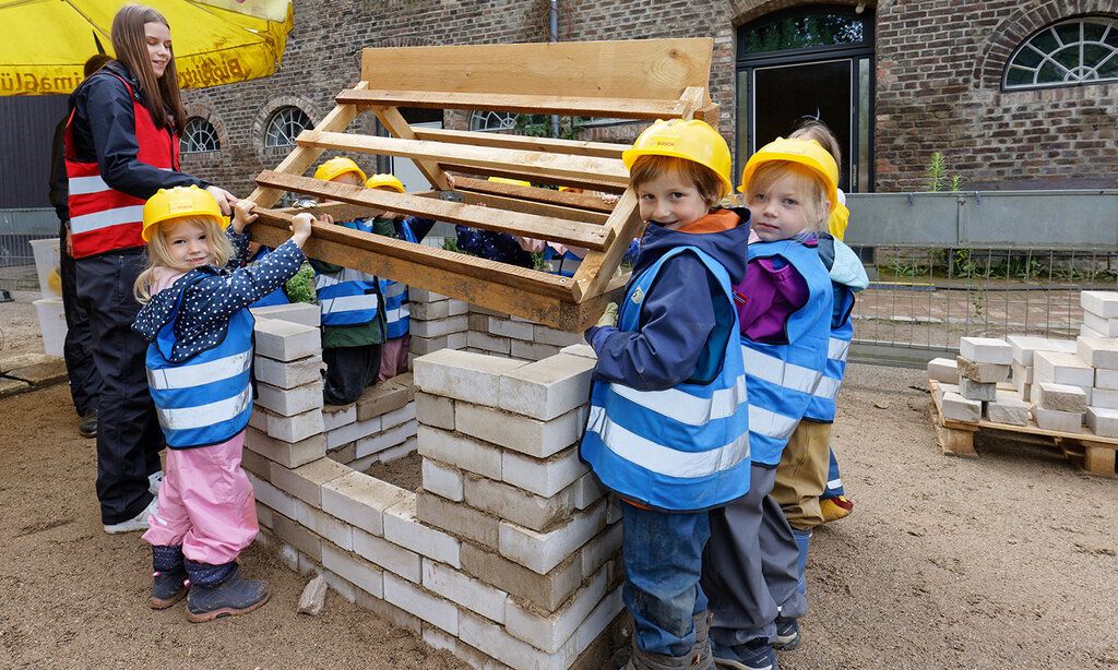 Kinder als kleine Bauarbeiter bauen das Dach von einem kleinen Haus