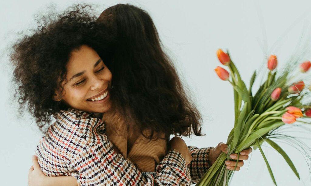 Mutter wird von Tochter umarmt und hält einen Strauß Tulpen in der Hand