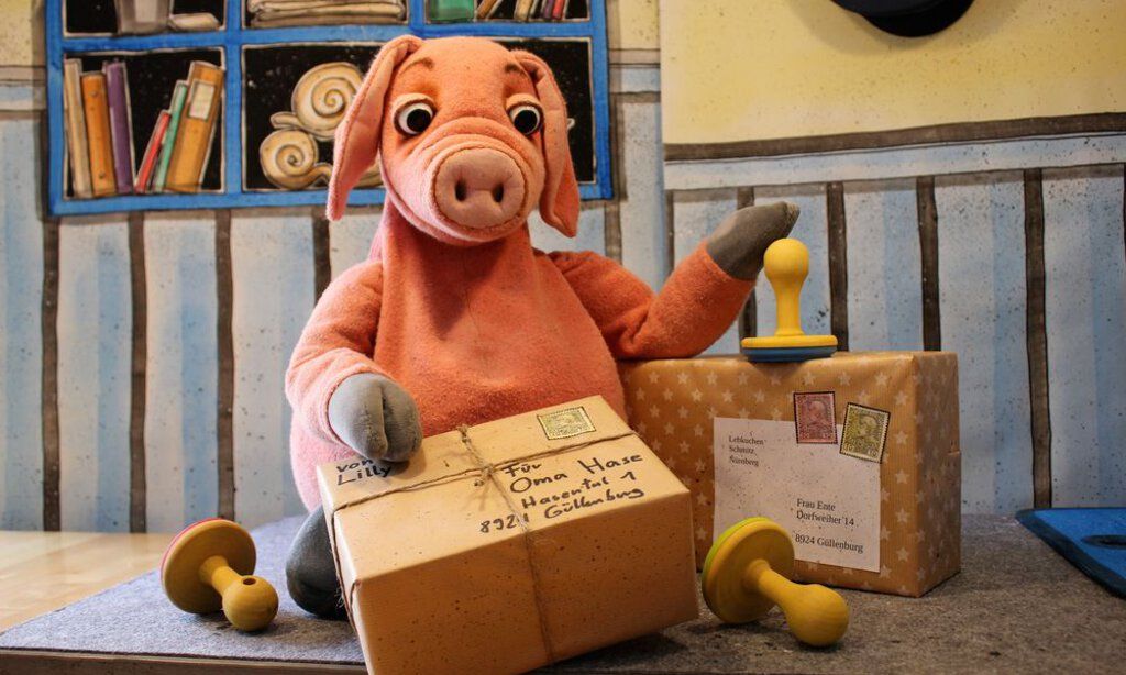 Das Schweinchen Rosa-Luise inmitten von Päckchen auf einem Postamt