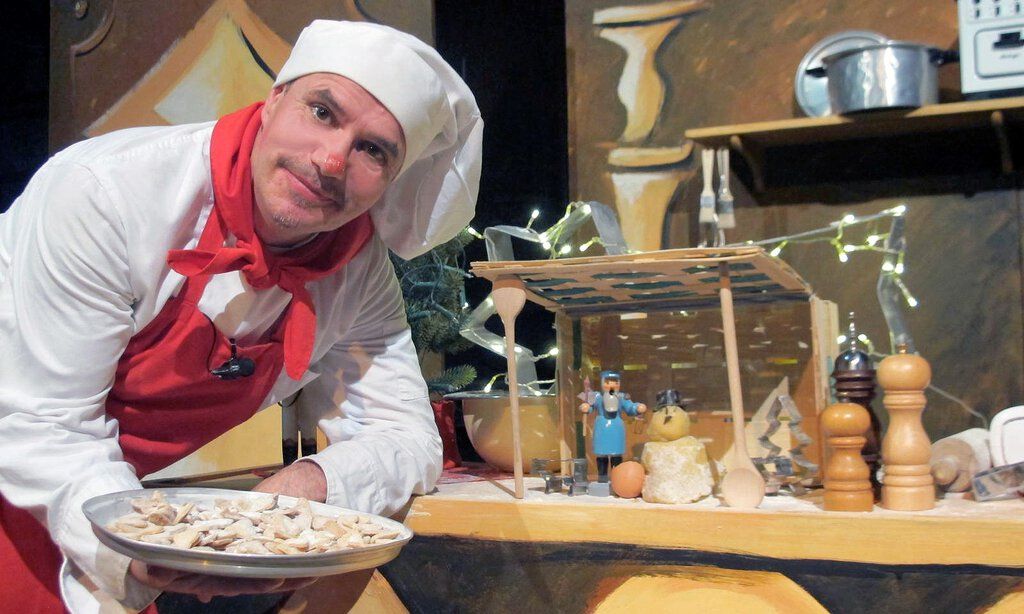 Tom Teuer steht in Kochuniform mit einem Teller Plätzchen in der Weihnachtsbäckerei