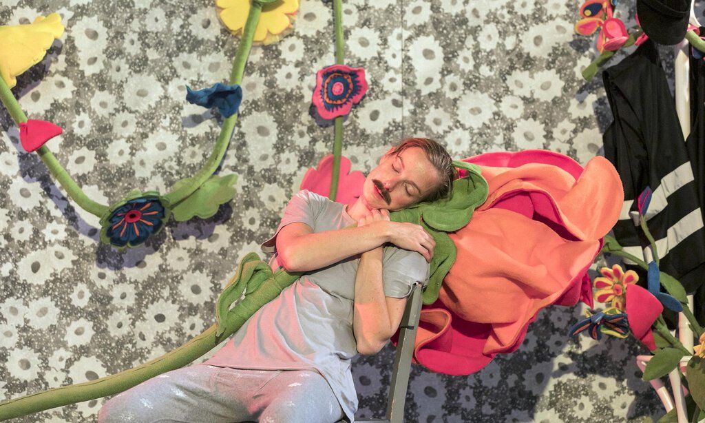 Ein Mann lehnt mit geschlossenen Augen an übergroßen Blumen.
