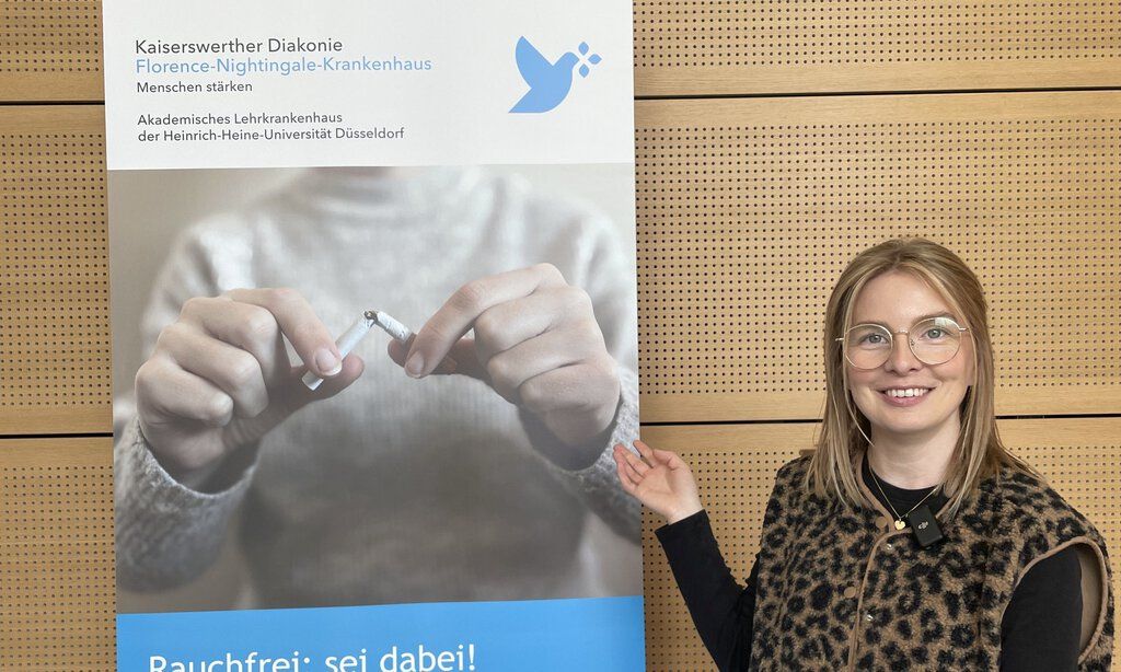 Frau lächelt in Kamera und deutet auf Plakat