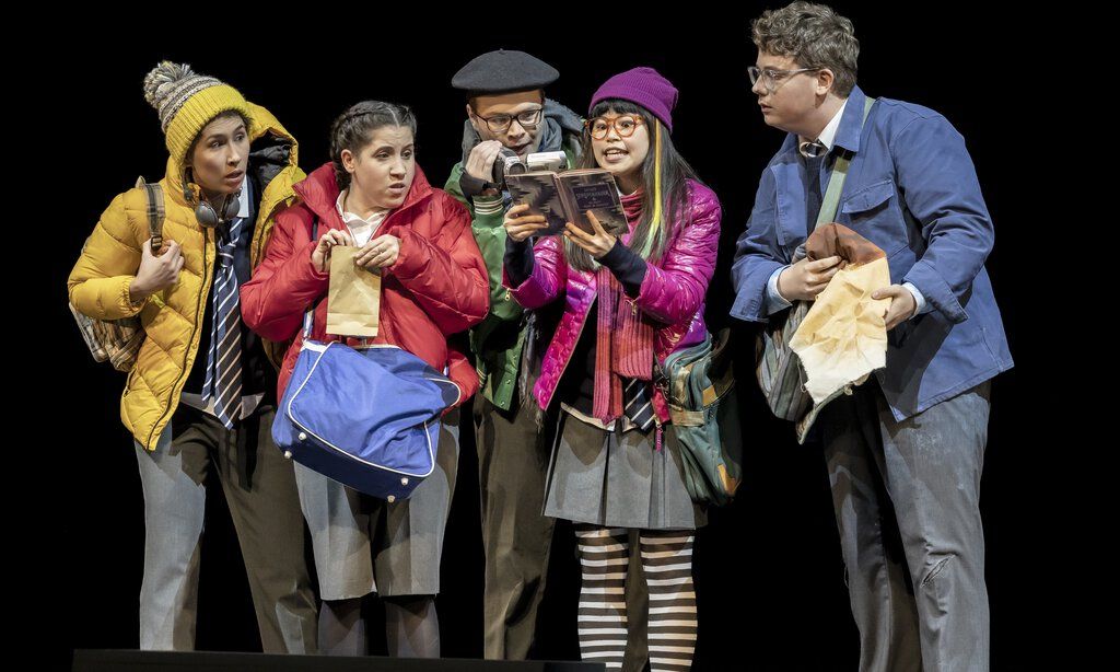 Fünf junge Schauspieler in „Das flegende Klassenzimmer“ schauen gebannt auf ein aufgeschlagenes Buch.