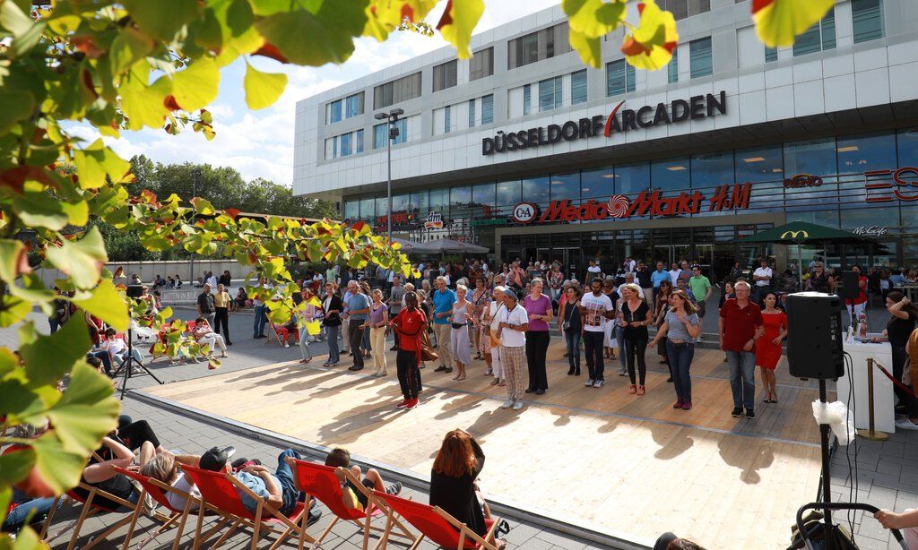 Menschengruppe tanzt in Formation vor einem Einkaufszentrum