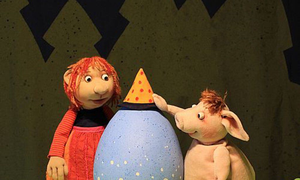 Eine kleine Hexe und ein Schweinchen bewundern ein himmelblaues großes Ei in ihrer Mitte