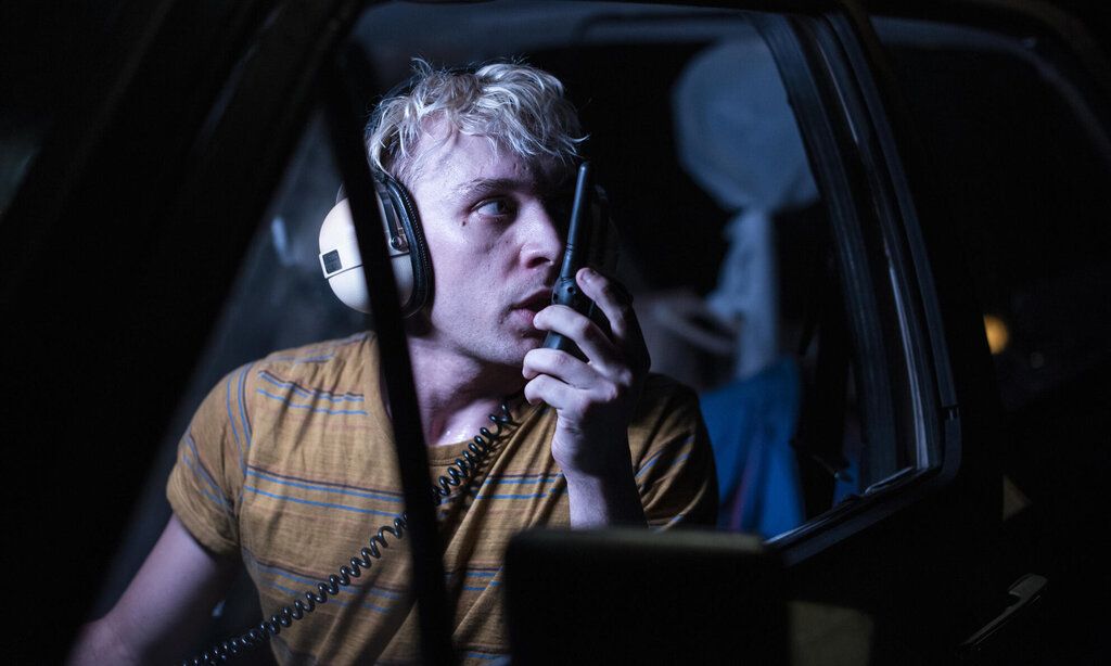 Ein Mann mit Kopfhörern sitzt im Dunkeln in seinem Auto und spricht in ein Funkgerät.