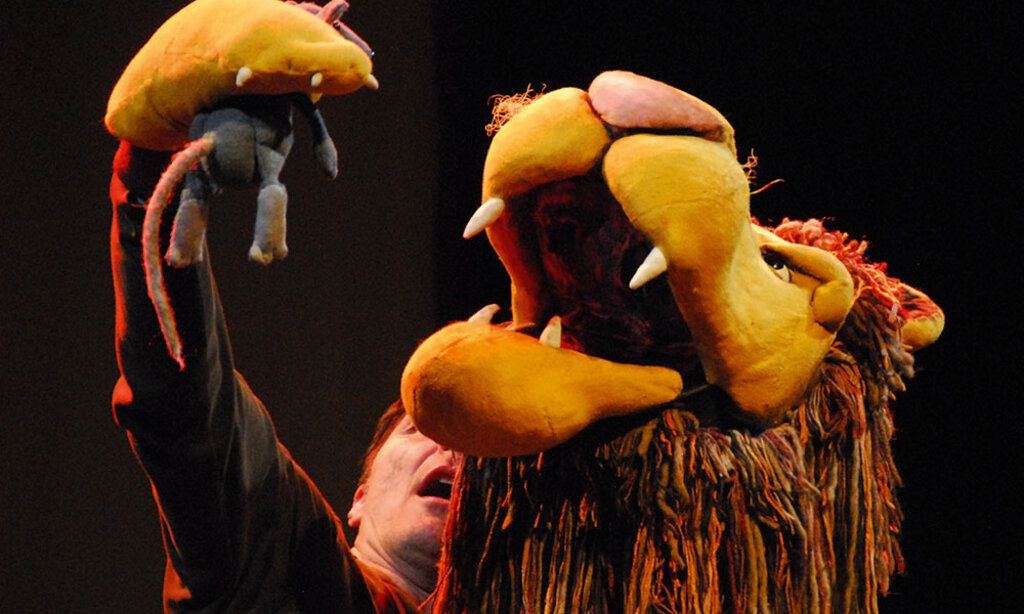 Eine Löwenpuppe des Figurentheaters Fithe hält in seiner Pranke eine Maus über sein geöffnetes Maul.