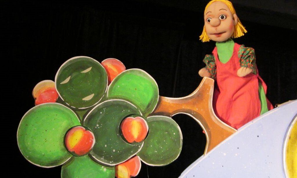 Die Goldmarie steht auf einer Puppenbühne vor dem Apfelbaum.