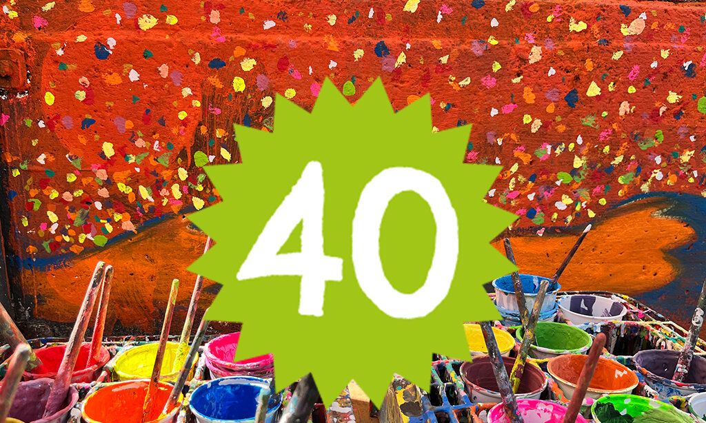 Die Zahl 40 ist vor einer bunten Konfetti.-Wand und Farbeimern platziert.