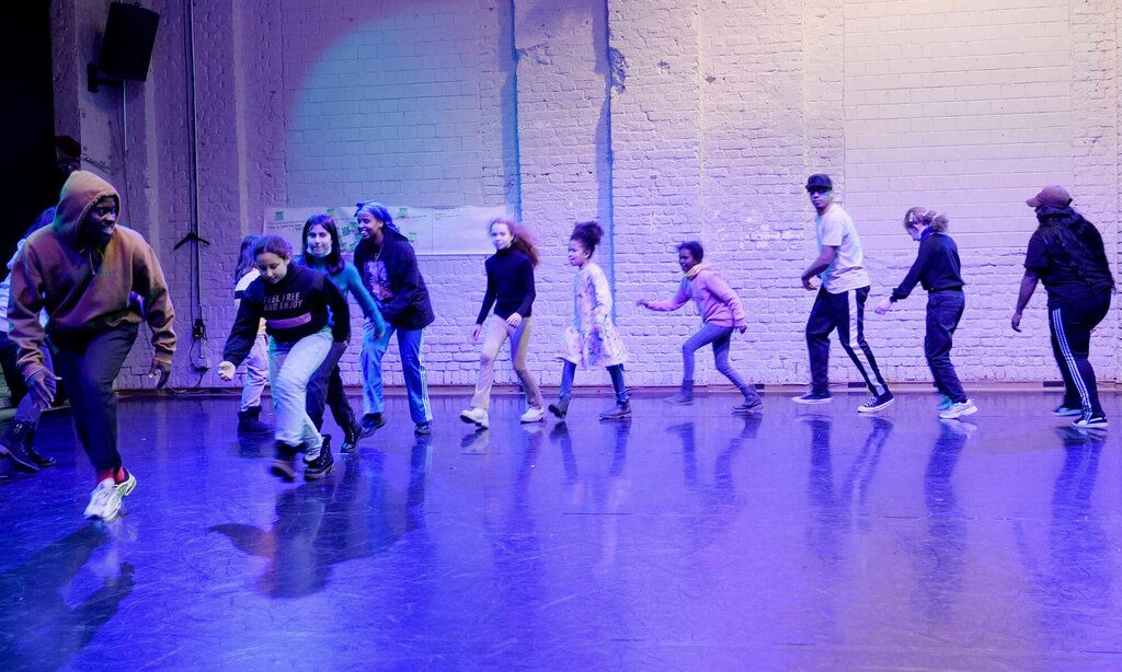 Ein Tänzer läuft gebückt mit Kindern ein einer Reihe über die Bühne.