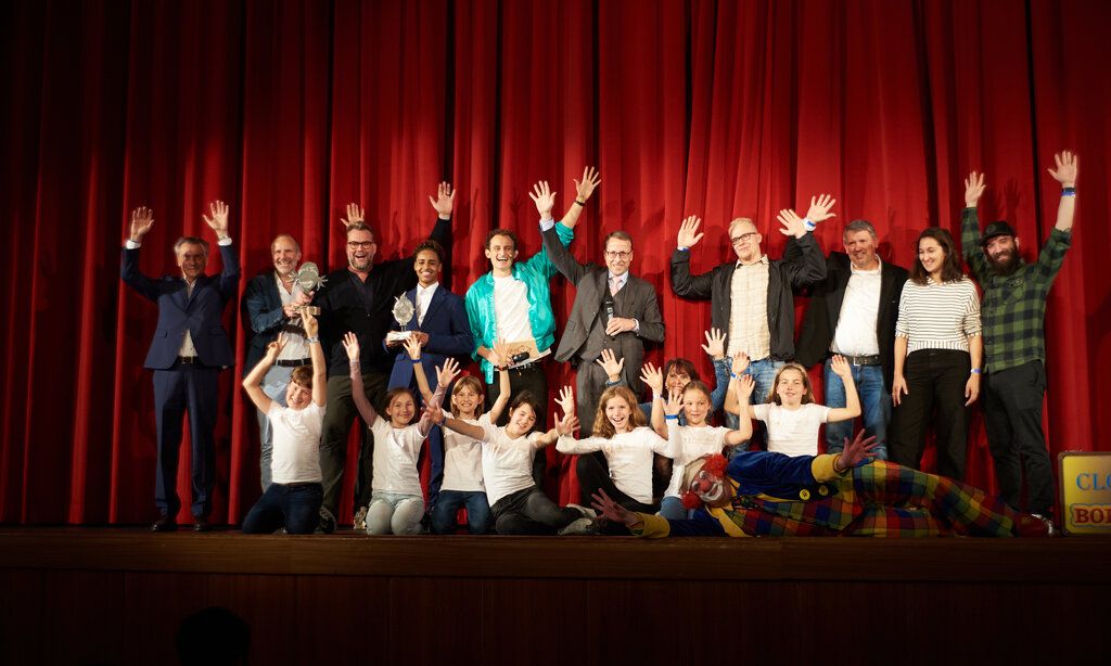 Jury und Preisträger der Kinderfilmtage im Ruhrgebiet von 2022 stehen auf der Bühne und winken in die Kamera.