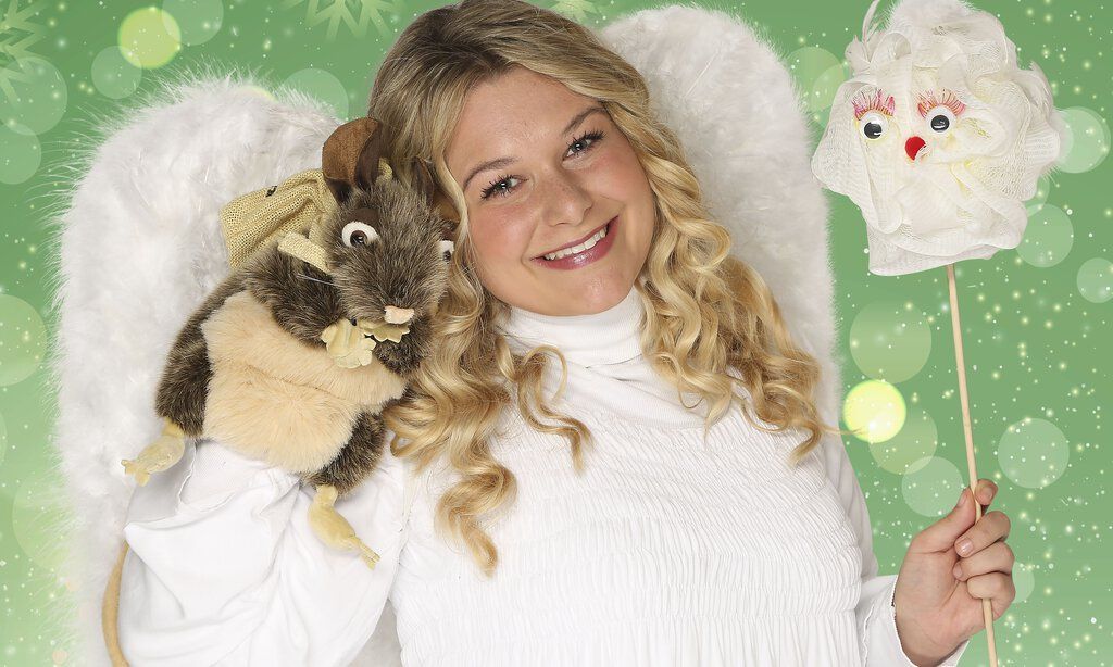 Ein blondes Mädchen lächelt als Engel verkleidet in die Kamera und hält eine Maus-Handpuppe in der Hand.