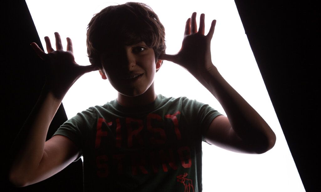 Ein Junge vor einer Lichtwand schaut feixend in die Kamera.