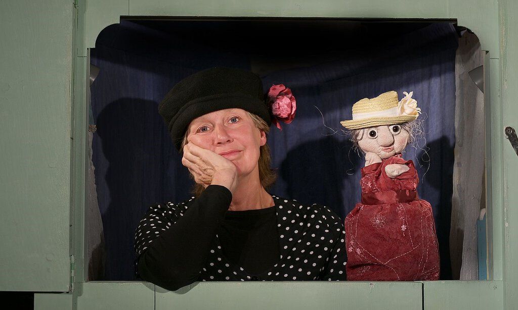 EIne Frau sitzt mit einer Handpuppe hinter einem Puppentheater