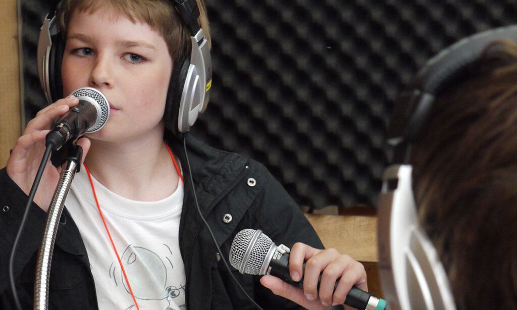 Ein Junge mit Kopfhörern in einem Tonstudio spricht ins Mikrofon.